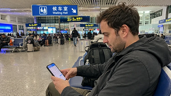 International traveler checking a high-speed train booking on a smartphone at a railway station in China